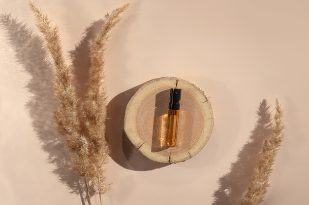 Parfümtester mit transparenter brauner Flüssigkeit auf einem Holzschnitt mit Pampasgras auf beigem Hintergrund - Foto, Bild