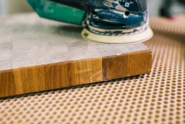 El carpintero pule la tabla de madera en el taller. El proceso de la rectificadora. Fabricación de muebles de madera. Molienda parcial - Foto, imagen