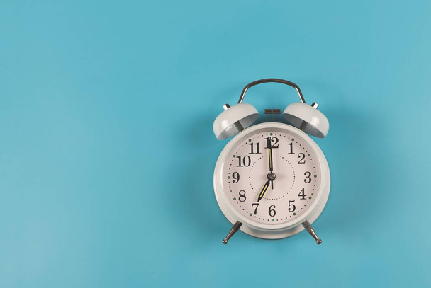 Top view or flat lay of white  vintage alarm clock shows 7 o clock  on blue  background. - Zdjęcie, obraz