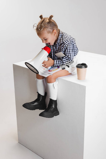 Обрезанный портрет милой маленькой девочки, кричащей в мегафон изолированы на сером фоне - Фото, изображение