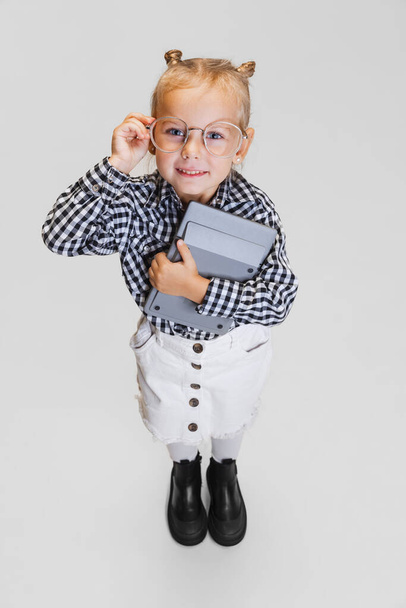 Ritratto ritagliato di carina bambina in abbigliamento casual e occhiali alla moda isolati su sfondo grigio - Foto, immagini
