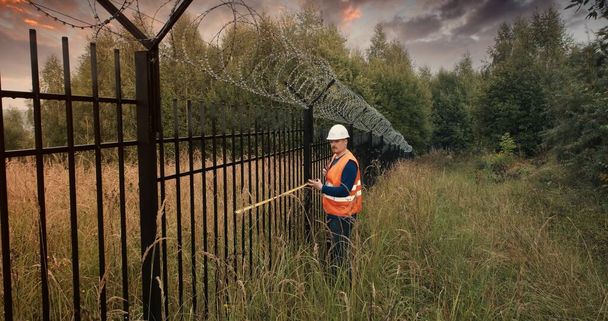 Trabajador con cinta métrica medir una valla con alambre de púas - Foto, imagen