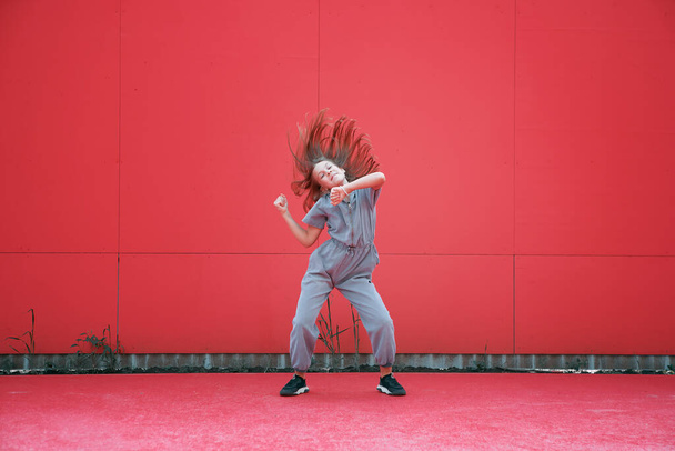Energetic teen girl dancing waving hair outdoors by red wall. Dancer performance. Contemporary dance school advertising - Fotó, kép