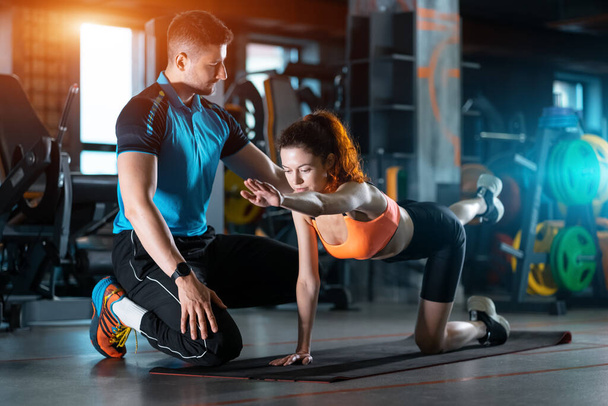 young woman exercising quadruplex with personal trainer in gym - Foto, afbeelding