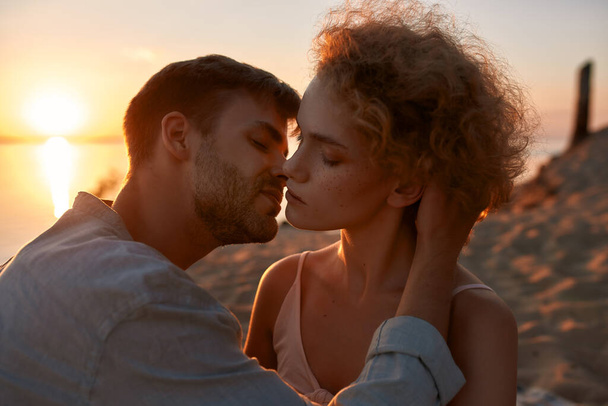 Two young people in love, couple looking passionate, kissing each other on the beach at sunset - Foto, immagini