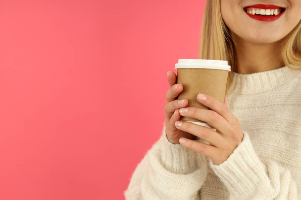 Attractive girl holds paper cup on pink background. - Фото, изображение