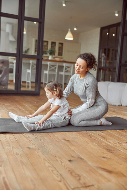 Smiling woman assisting daughter during home workout - Photo, Image