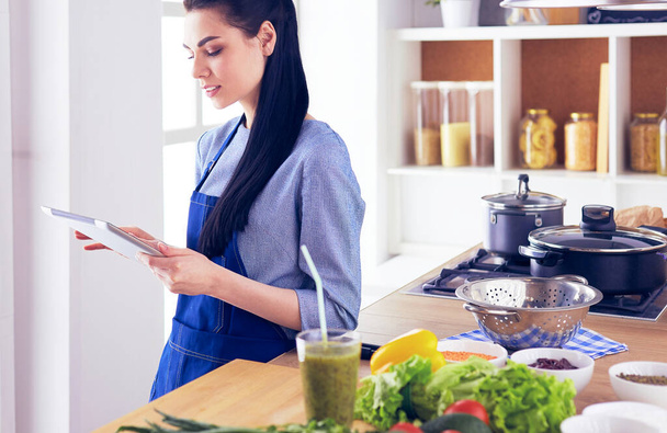 Young woman using a tablet computer to cook in her kitchen - Foto, Imagem