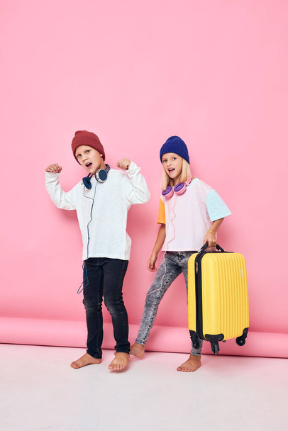 joyful boy and girl with a yellow suitcase in his hands studio posing - Foto, Imagem