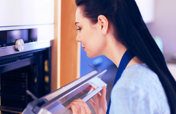 Beautiful young woman checking how her cake is doing in the oven - Photo, image