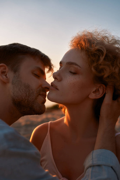 Beautiful young people in love, couple looking passionate, kissing each other on the beach at sunset - Fotoğraf, Görsel