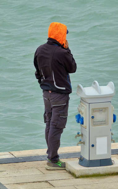 Włochy, Sycylia, Morze Śródziemne, Marina di Ragusa (prowincja Ragusa); mężczyzna przy telefonie w porcie  - Zdjęcie, obraz