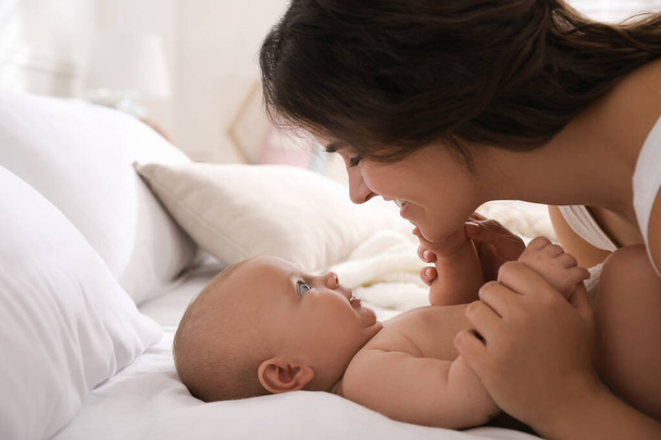 Happy young mother with her cute baby on bed indoors - Photo, Image