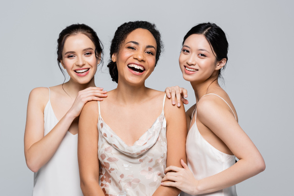 Smiling multiethnic women posing and looking at camera isolated on grey  - Foto, Bild