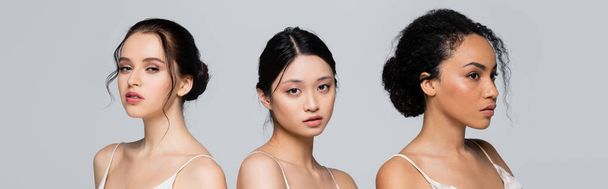 Pretty asian woman looking at camera near multiethnic friends isolated on grey, banner  - Photo, image