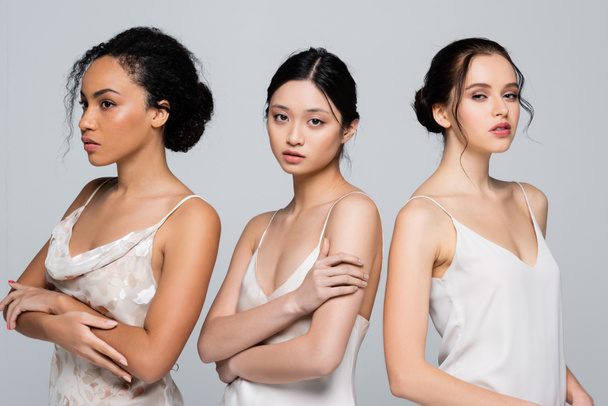 Pretty asian woman in satin dress standing near multiethnic women isolated on grey  - Photo, Image