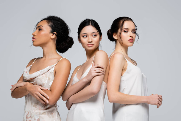Young interracial women in satin dresses posing isolated on grey  - 写真・画像