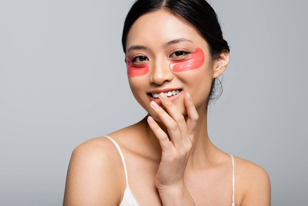 Pretty asian woman with eye patches smiling at camera isolated on grey  - Foto, immagini
