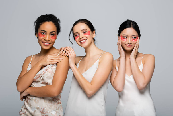 Smiling multiethnic women with eye patches looking at camera isolated on grey  - Foto, Imagem