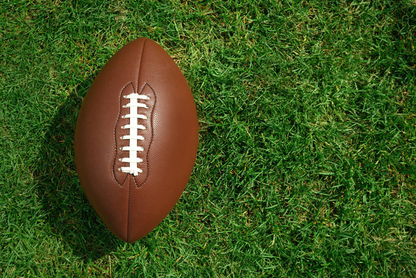 American football ball on green grass, top view. Space for text - Valokuva, kuva
