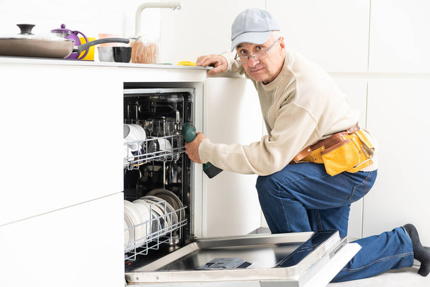 Uitzicht op de mens in het algemeen reparatie afwasmachine in de keuken - Foto, afbeelding
