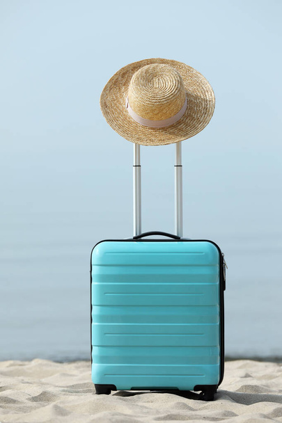 Turquoise suitcase with straw hat on sandy beach - Foto, afbeelding