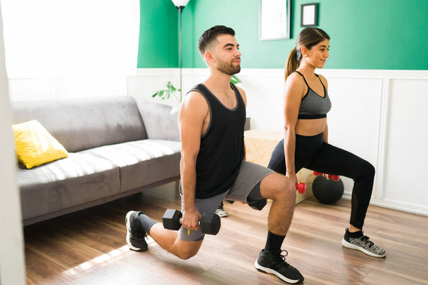 Glückliche lateinische Männer und Frauen beim Ausfallschritt mit Gewichten. Fittes Paar beim Training mit Kurzhanteln - Foto, Bild