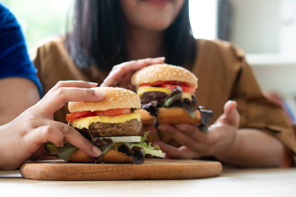 空腹太りすぎの女性は、木製のプレート上にハンバーガーを保持します,自宅からの仕事中に,体重の問題を得る.大食障害の概念(BED). - 写真・画像