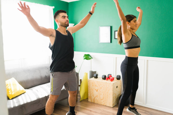 Fitness couple. Active woman and man doing a high intensity interval training at home and exercising with jumping jacks - 写真・画像