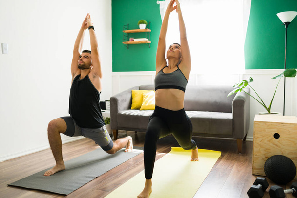 Doing yoga to start the day. Fitness couple in sportswear in a crescent lung pose in the living room - Fotografie, Obrázek
