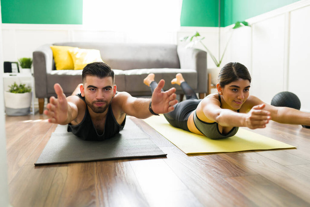 Attractive workout partners in a locust pose working out with yoga exercises in the living room  - Photo, Image
