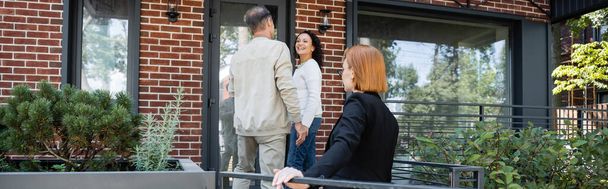 redhead realtor standing behind interracial couple near modern house, banner - Photo, Image
