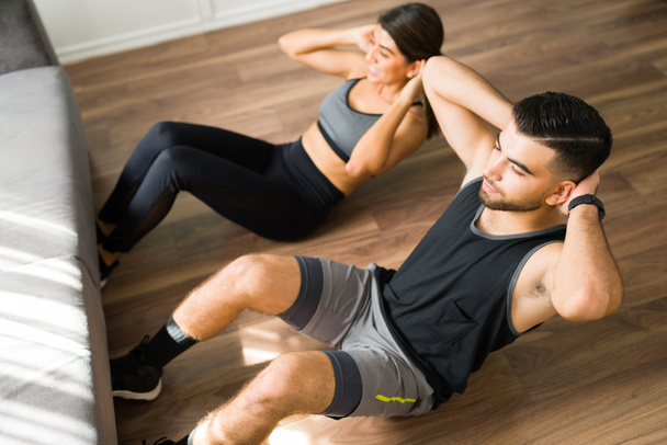 Staying fit together. High angle of an active man and woman doing abdominal crunches together  - Photo, Image