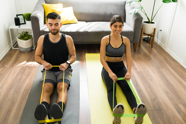 Attractive boyfriend and girlfriend staying fit together. Young woman and man exercising with resistance bands - Photo, Image