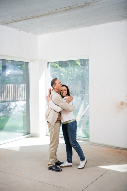 alegre hombre abrazando complacido africano americano esposa en nuevo casa - Foto, Imagen