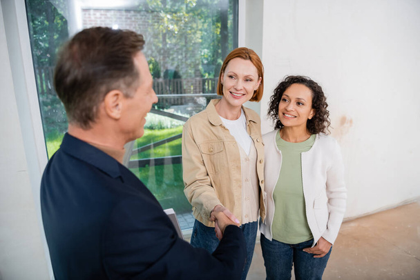 blurred realtor shaking hands with happy redhead woman near african american girlfriend  - Photo, Image