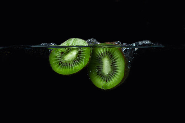 Kiwi padá do vody na černém pozadí. Zralé a chutné kiwi. Kiwi cutaway - Fotografie, Obrázek