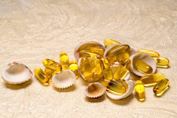Omega-3 fish fat oil capsules heap lie on the small shells as a treasure. Copy space for your text. EPA and DHA are essential fatty substances that our bodies need on a daily basis. - Photo, Image