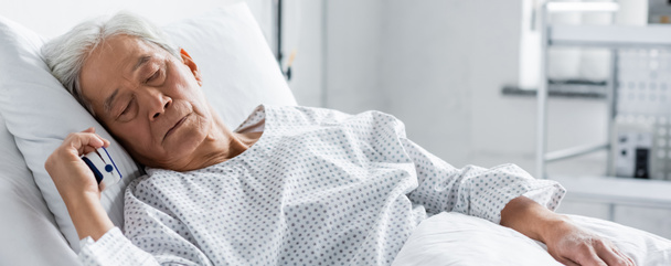 Ηλικιωμένος Ασιάτης ασθενής με παλμικό οξύμετρο κοιμάται στο κρεβάτι στην κλινική, πανό  - Φωτογραφία, εικόνα