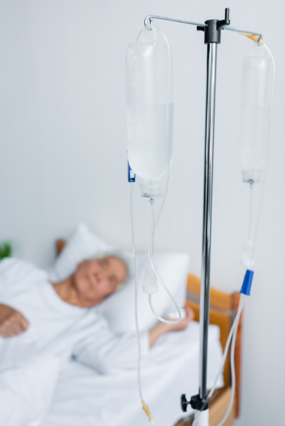 Intravenous therapy stand near blurred patient on bed in hospital  - Foto, imagen