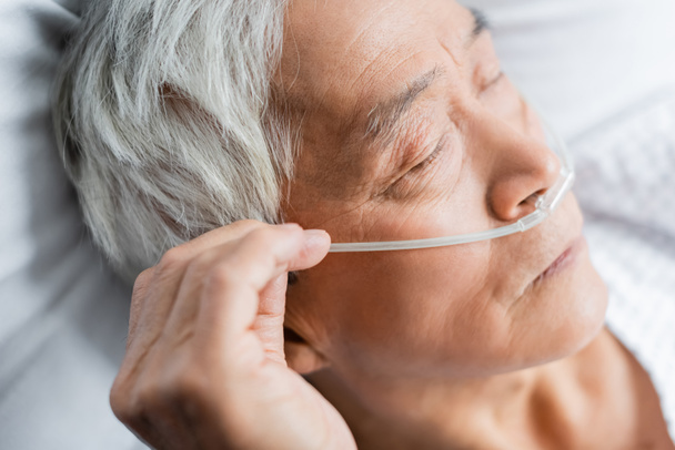Anziani asiatici con cannula nasale sdraiati con gli occhi chiusi sul letto in clinica  - Foto, immagini