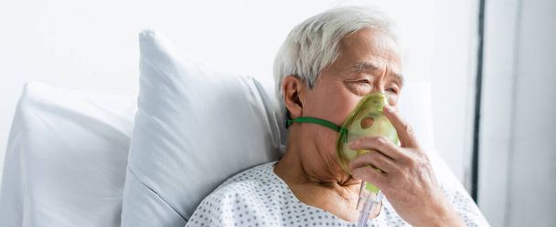 Senior Aziatische patiënt met zuurstofmasker zittend op bed in kliniek, spandoek  - Foto, afbeelding