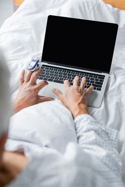 Niewyraźny pacjent z oksymetr pulsacyjny przy użyciu laptopa z pustym ekranem na łóżku  - Zdjęcie, obraz