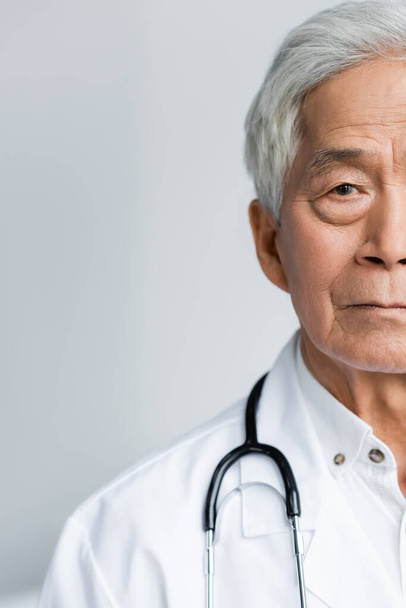 Обрезанный вид пожилого азиатского врача, смотрящего на камеру в больнице   - Фото, изображение