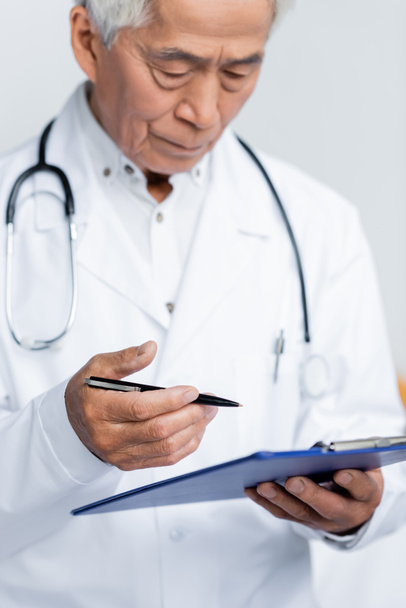 Blurred asian doctor holding pen and clipboard in clinic  - Photo, Image