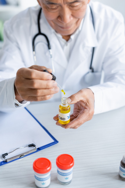 Asian doctor holding cbd oil near medical cannabis and clipboard in clinic  - Фото, зображення