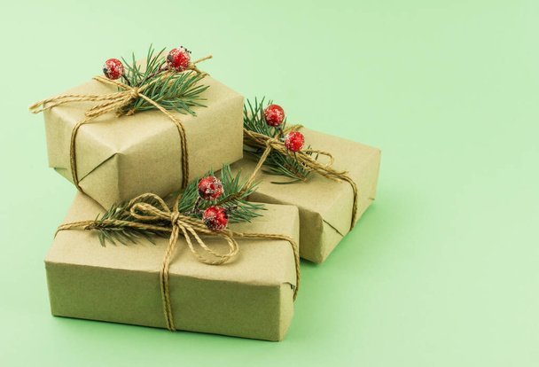 three boxes of gifts in craft paper with decor of spruce branches and berries on a green background - Foto, Imagen