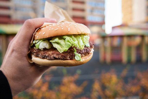 Big Burger in der Hand eines Mannes auf verschwommenem Hintergrund - Foto, Bild