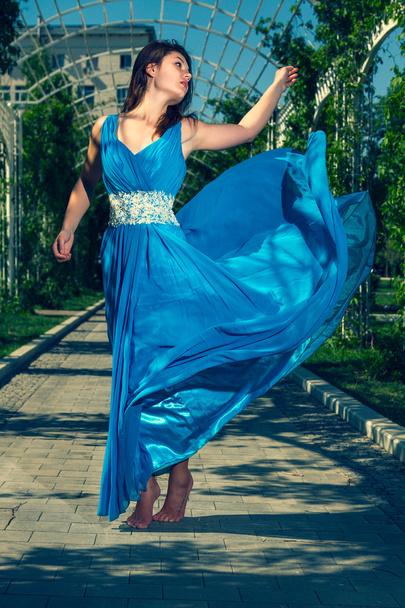 Beautiful woman dancing barefoot in a long blue dress - Фото, зображення