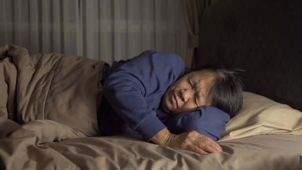 Sleepy oudere oude Aziatische vrouw. Mensen liggen en slapen op bed in de slaapkamer 's avonds laat thuis. Levensstijl - Foto, afbeelding